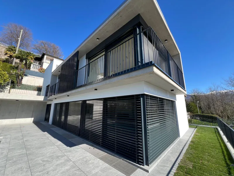 Casa contemporanea con facciata bianca, frangisole antracite e balcone in cemento
